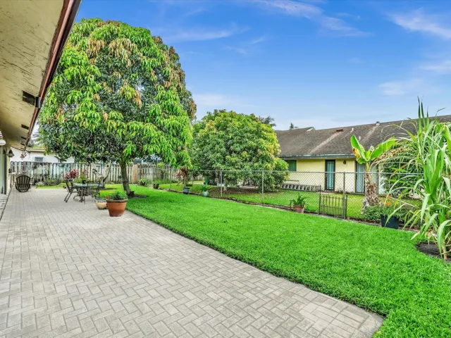 Paved patio and backyard lawn with mature trees, fenced space, and room for outdoor seating or entertaining.