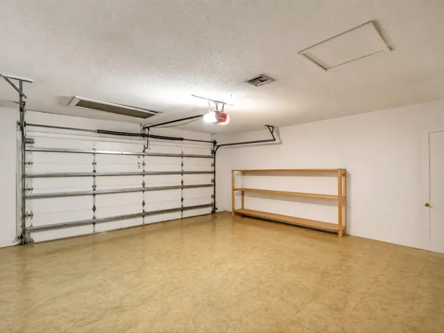 Two-car garage interior with garage door, storage area, workbench, and parking space at 8330 NW 54th St.