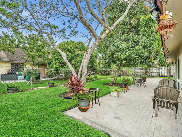 Large backyard with patio seating, mature trees, green lawn, and fenced outdoor space at this Lauderhill home.
