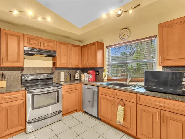 Kitchen sink and dishwasher area with wood cabinets, stainless appliances, window light, and practical workspace.