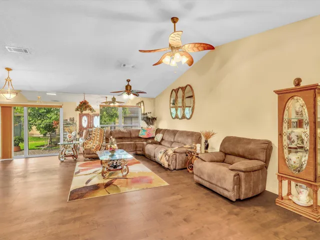 Wide living room view showing the open main living space, front windows, ceiling fan, and comfortable seating area.