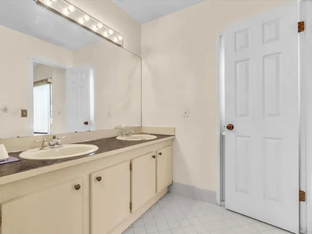 Primary bathroom vanity view with mirror, sink, countertop, light fixture, and clean neutral finishes.