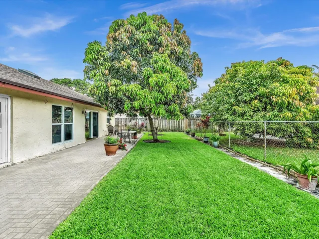 Backyard view showing green lawn, paved patio area, mature trees, and the rear exterior wall of the single-family home.