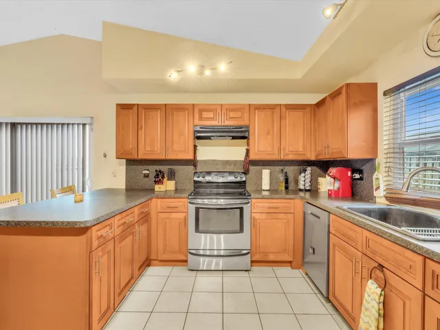 Kitchen view with stainless stove, wood cabinets, tile flooring, and a window that brings in natural light near the sink area.