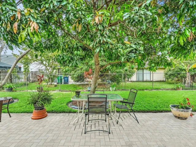 Back patio and yard with paved seating area, mature trees, fenced outdoor space, and shaded areas for relaxing outside.
