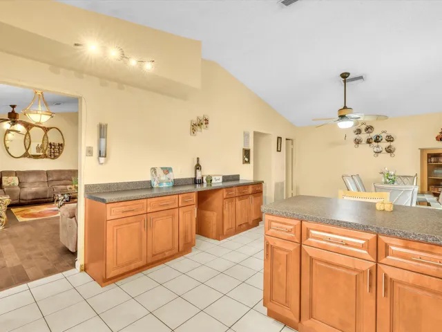 Edited kitchen bar view showing wood cabinetry, tile floors, breakfast bar space, and open connection to the dining area.