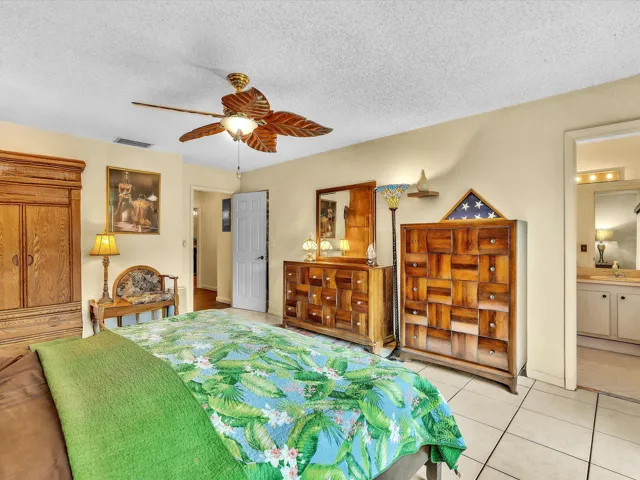 Primary bedroom angle showing tile flooring, ceiling fan, bed area, built-in storage, and access toward the ensuite bath.
