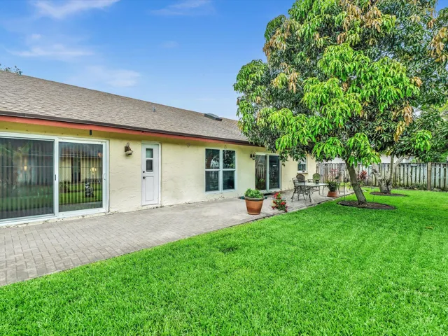 Rear exterior view with backyard lawn, mature tree, windows, fencing, and open outdoor space behind the home.