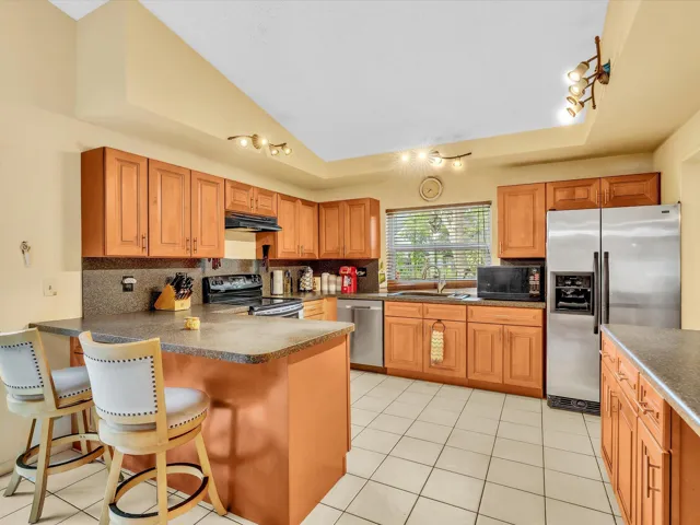 Updated kitchen in this Lauderhill home with wood cabinets, stainless appliances, tile floors, and a long breakfast bar.