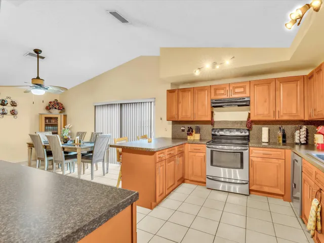 Edited kitchen and dining area view showing wood cabinetry, tile flooring, counter space, and the open connection between rooms.