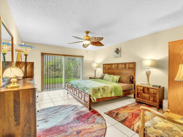 Primary bedroom with tile flooring, ceiling fan, large window, sliding glass doors, and a spacious layout.