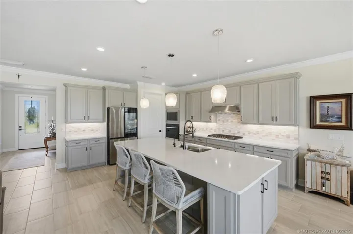 Designer gourmet kitchen showcases an oversized quartz island with seating, upgraded cabinetry, stainless steel appliances, built-in wall oven, gas cooktop, and stylish tile backsplash. Open to the main living areas, this beautifully appointed kitchen is perfect for entertaining, casual dining, and everyday living.