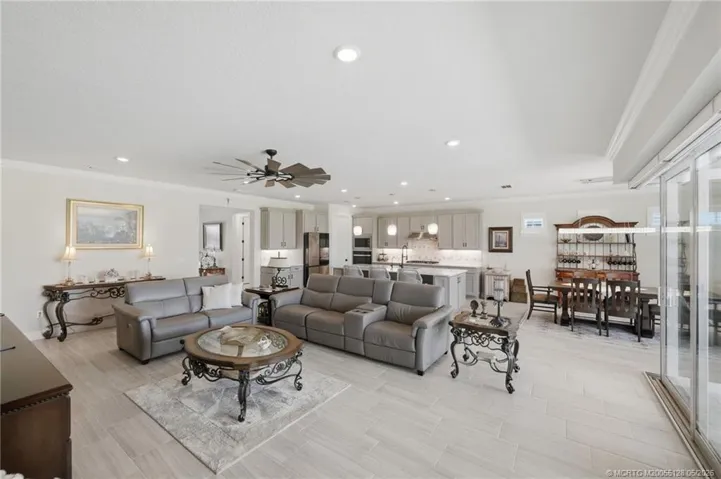 Expansive open floor plan offers seamless flow between the living, dining, and kitchen areas, creating the perfect space for entertaining and everyday living. Features include elegant tile flooring, crown molding, recessed lighting, and large sliding glass doors that fill the home with natural light and connect to the outdoor living area and pool.