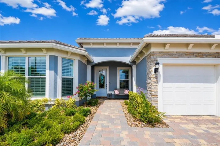 Inviting covered entry welcomes you to this beautifully maintained 3-bedroom, 3-bath home in Del Webb at Tradition. Enjoy impressive curb appeal with upgraded stone accents, elegant paver walkway and driveway, manicured tropical landscaping, and a charming front sitting area perfect for relaxing and greeting guests. Thoughtfully designed with quality finishes and located in one of Tradition’s premier active adult communities.