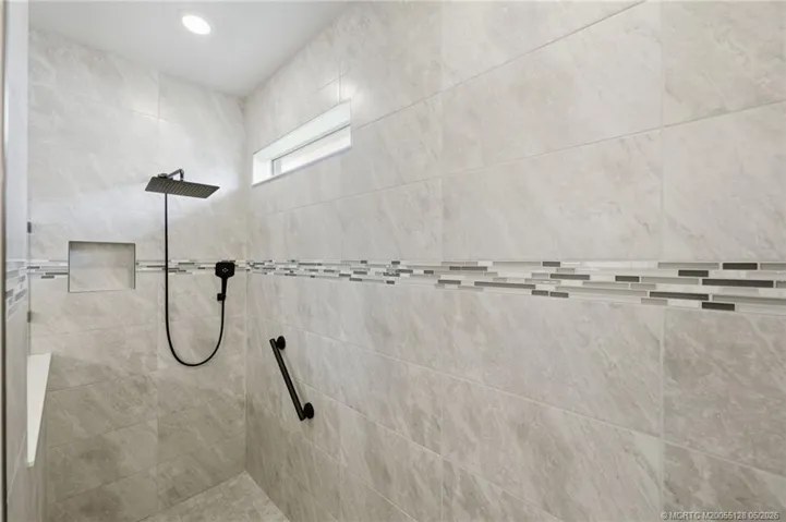 Oversized walk-in primary shower showcases elegant floor-to-ceiling tile, designer accent trim, built-in niche, and upgraded rainfall showerhead. This beautifully finished spa-inspired space offers a luxurious and relaxing retreat with modern style and exceptional attention to detail.