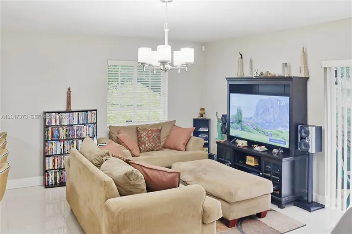 Living area featuring polished tile flooring, a multi-arm chandelier, and white horizontal window blinds