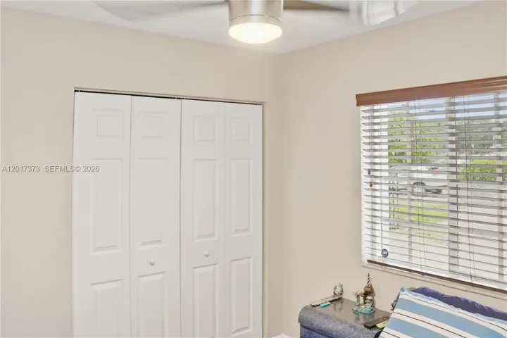 Neutral-toned interior featuring a multi-panel bi-fold closet, a ceiling-mounted light fixture with a fan, and a window with horizontal slatted blinds