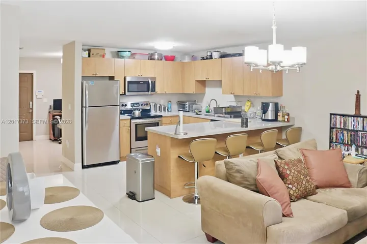 Kitchen featuring light wood cabinetry, stone countertops, stainless steel appliances, a breakfast bar, and a multi-light pendant fixture