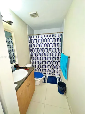 Bathroom featuring a wood-finish vanity with a stone-surfaced countertop, an integrated oval sink, ceramic tile flooring, and a shower-tub combination with a wall-mounted fixture
