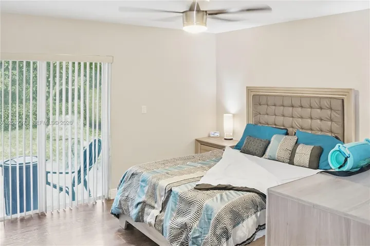 Sliding glass door with vertical blinds, wood-finish flooring, and a modern ceiling fan with integrated lighting