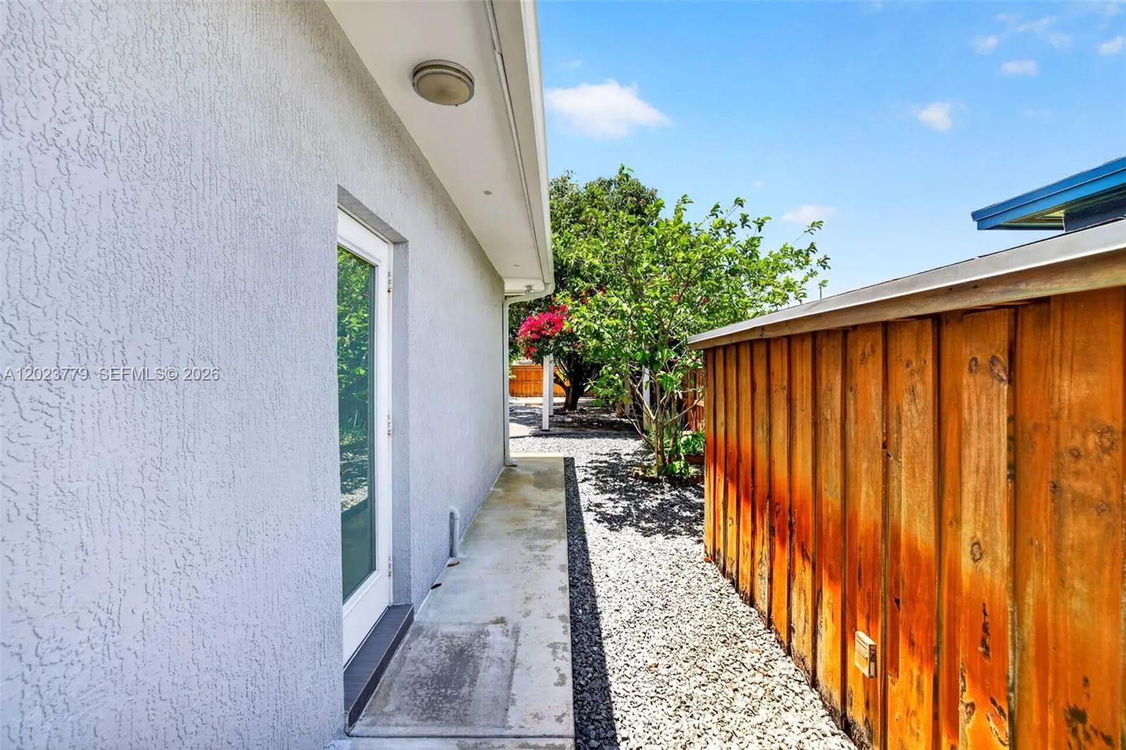 Side door from garage to the storage shed next to the house. Notice the long concrete pad to take you to backyard, and gravel and stone chips