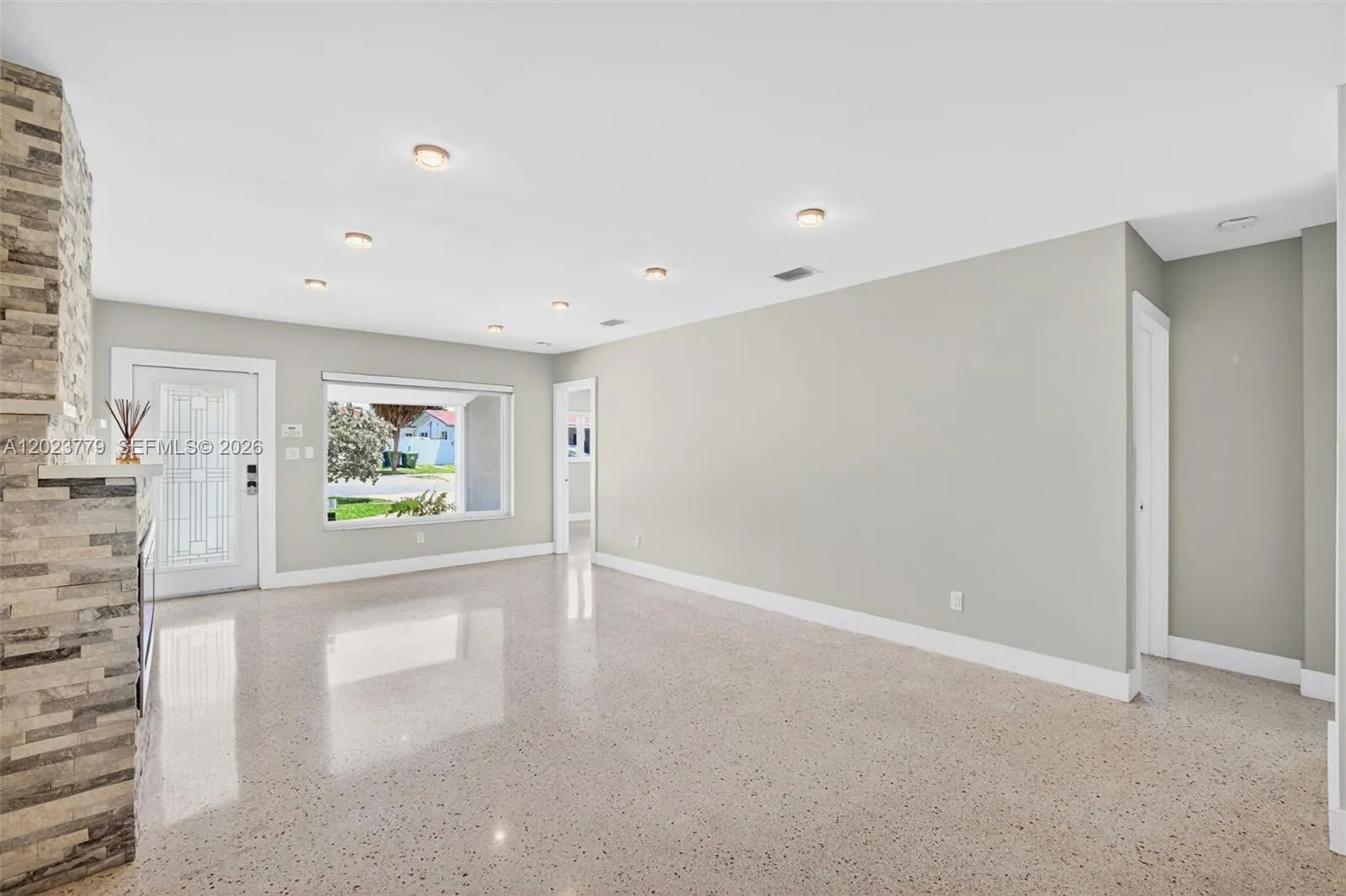 Stacked Stone Electric Fireplace with color changing light, lots of high hat lighting, beautiful restored polished terrazzo flooring. Flat ceilings and neutral beautiful paint, large impact window overlooking front yard. Hallway on right leads to two guest bedrooms