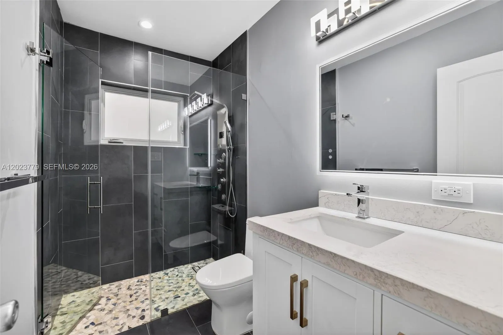 Guest bathroom w/ river rock look shower floor, frameless glass shower enclosure, floor to ceiling tile in shower, backlit mirror, solid surface counter and upgraded floor and vanity, w/ multifunction shower head