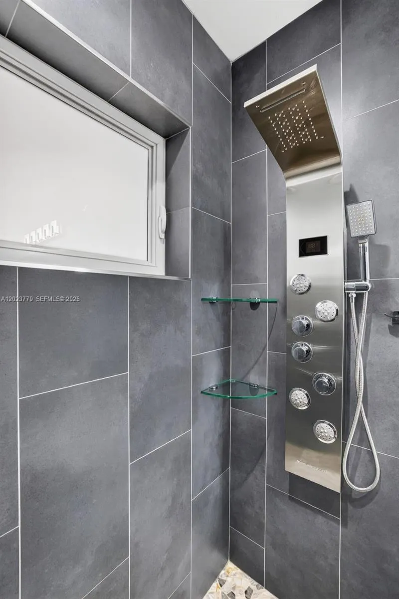 Guest bathroom w/ river rock look shower floor, frameless glass shower enclosure, floor to ceiling tile in shower, backlit mirror, solid surface counter and upgraded floor and vanity, w/ multifunction shower head