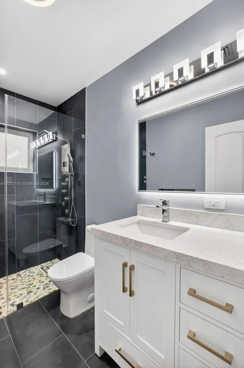 Guest bathroom w/ river rock look shower floor, frameless glass shower enclosure, floor to ceiling tile in shower, backlit mirror, solid surface counter and upgraded floor and vanity, w/ multifunction shower head