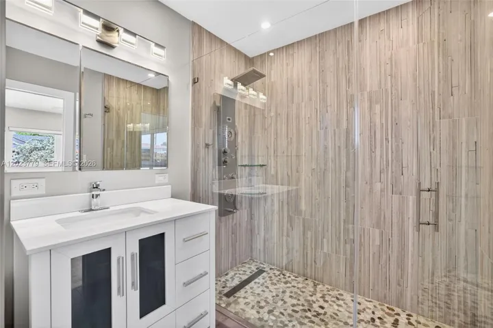Primary bathroom w/ frameless glass enclosure, river rock look tile, floor to ceiling wood look plank tile, medicine cabinet and upgraded vanity and flooring