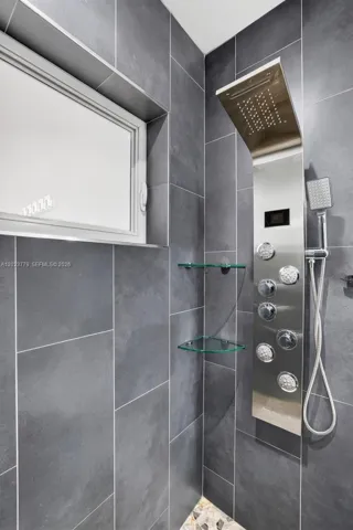 Guest bathroom w/ river rock look shower floor, frameless glass shower enclosure, floor to ceiling tile in shower, backlit mirror, solid surface counter and upgraded floor and vanity, w/ multifunction shower head