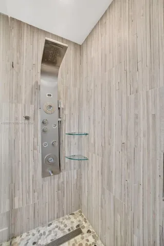 Primary bathroom w/ frameless glass enclosure, river rock look tile, multi function shower head, floor to ceiling wood look plank tile, medicine cabinet and upgraded vanity and flooring