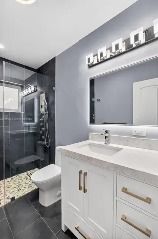 Guest bathroom w/ river rock look shower floor, frameless glass shower enclosure, floor to ceiling tile in shower, backlit mirror, solid surface counter and upgraded floor and vanity, w/ multifunction shower head