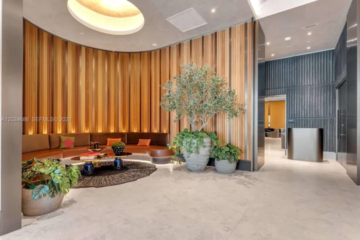 Curved wood-slat wall feature with integrated recessed lighting, large-format stone-finish floor tiling, circular recessed ceiling detail, and metallic accent wall paneling