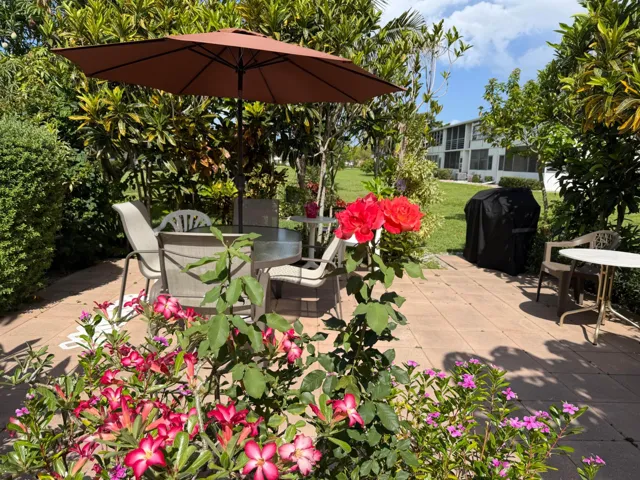 Looking out from front door is outdoor patio with flowers, table, chairs and grill right outside of the front door.