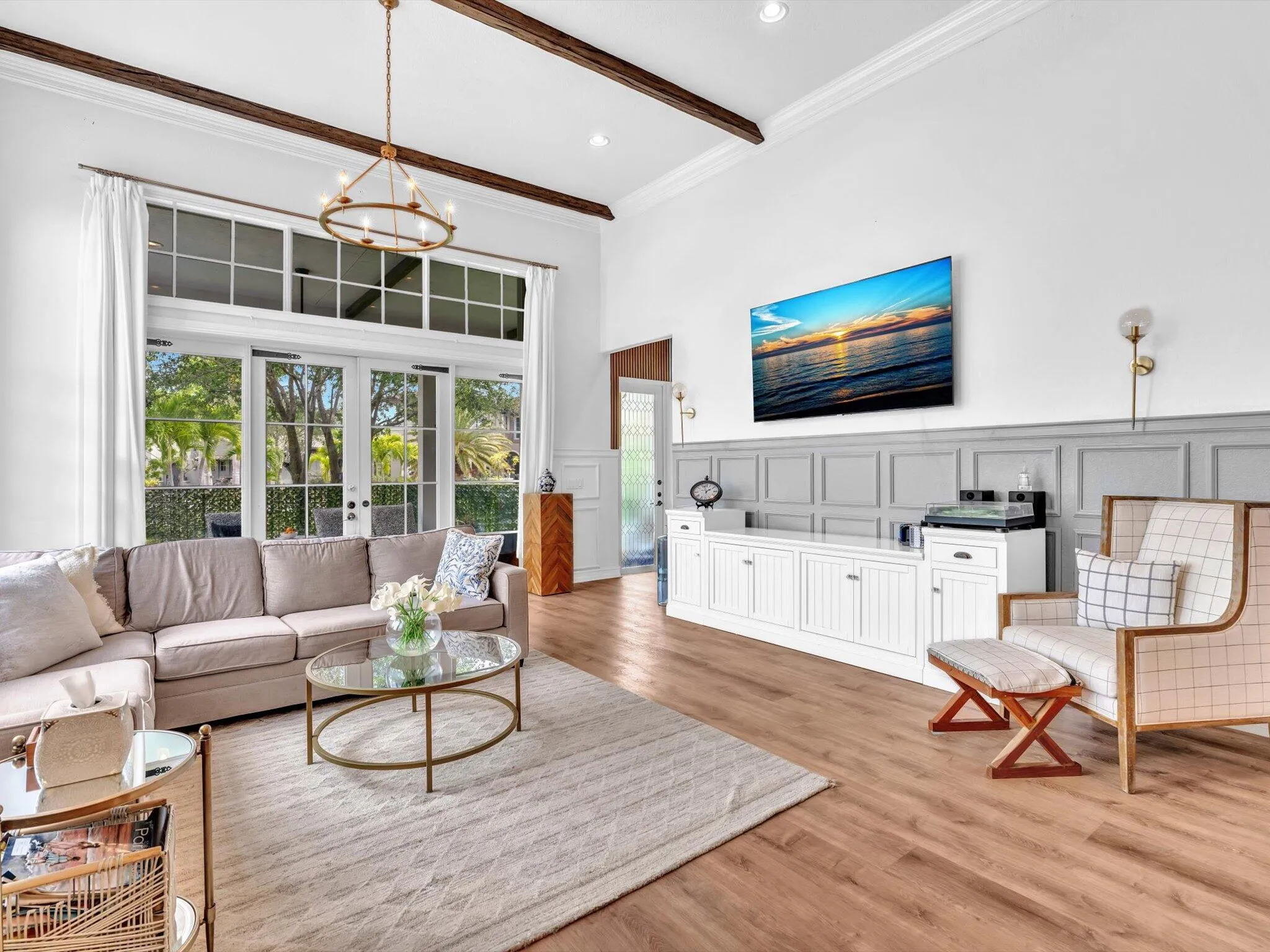 THIS OVERSIZED FAMILY ROOM WITH BEAM CEILINGS WAINSCOTTING AND GLASS DOORS LEADING TO COVERED PATIO