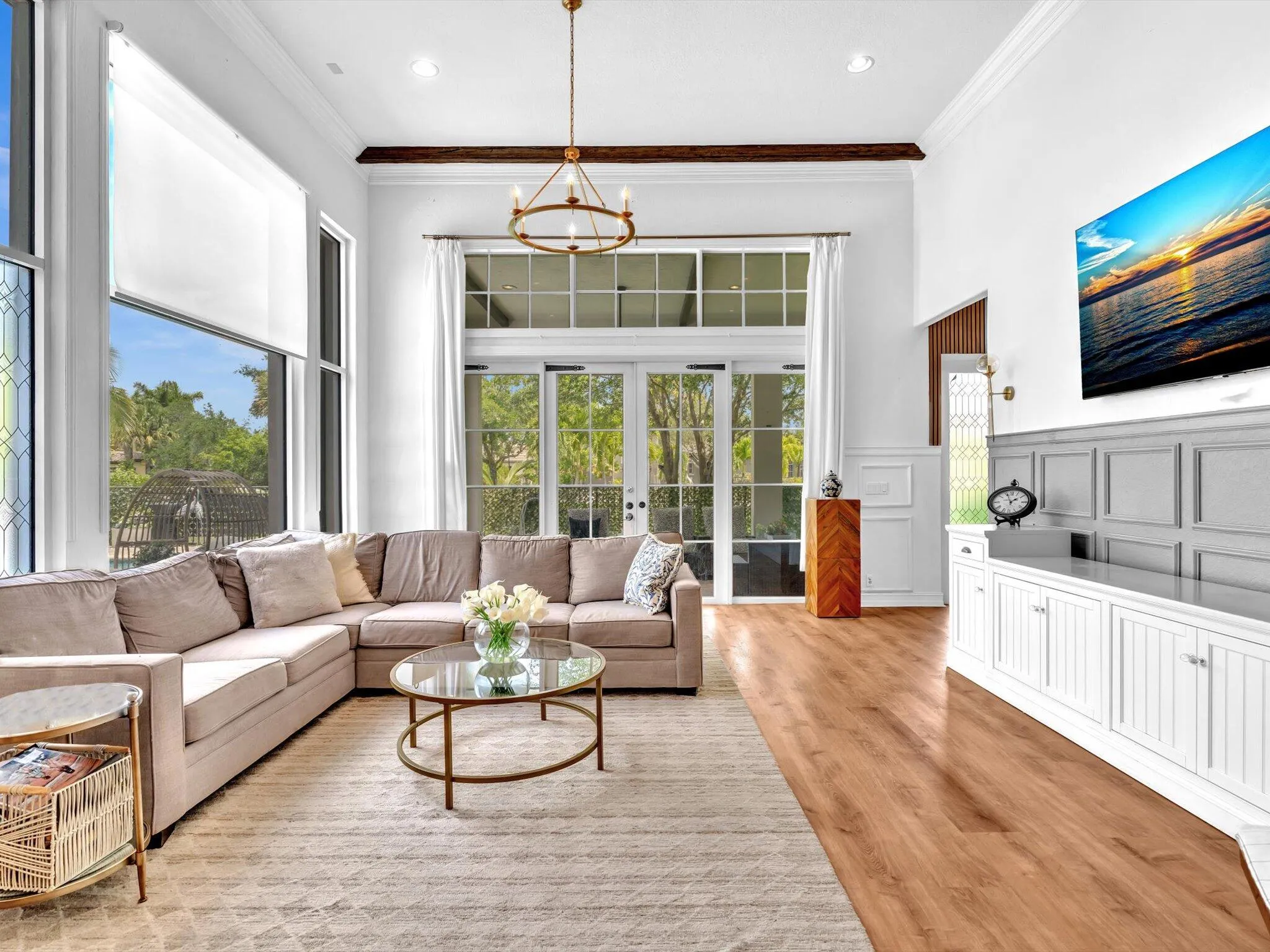 THIS OVERSIZED FAMILY ROOM WITH BEAM CEILINGS WAINSCOTTING AND GLASS DOORS LEADING TO COVERED PATIO