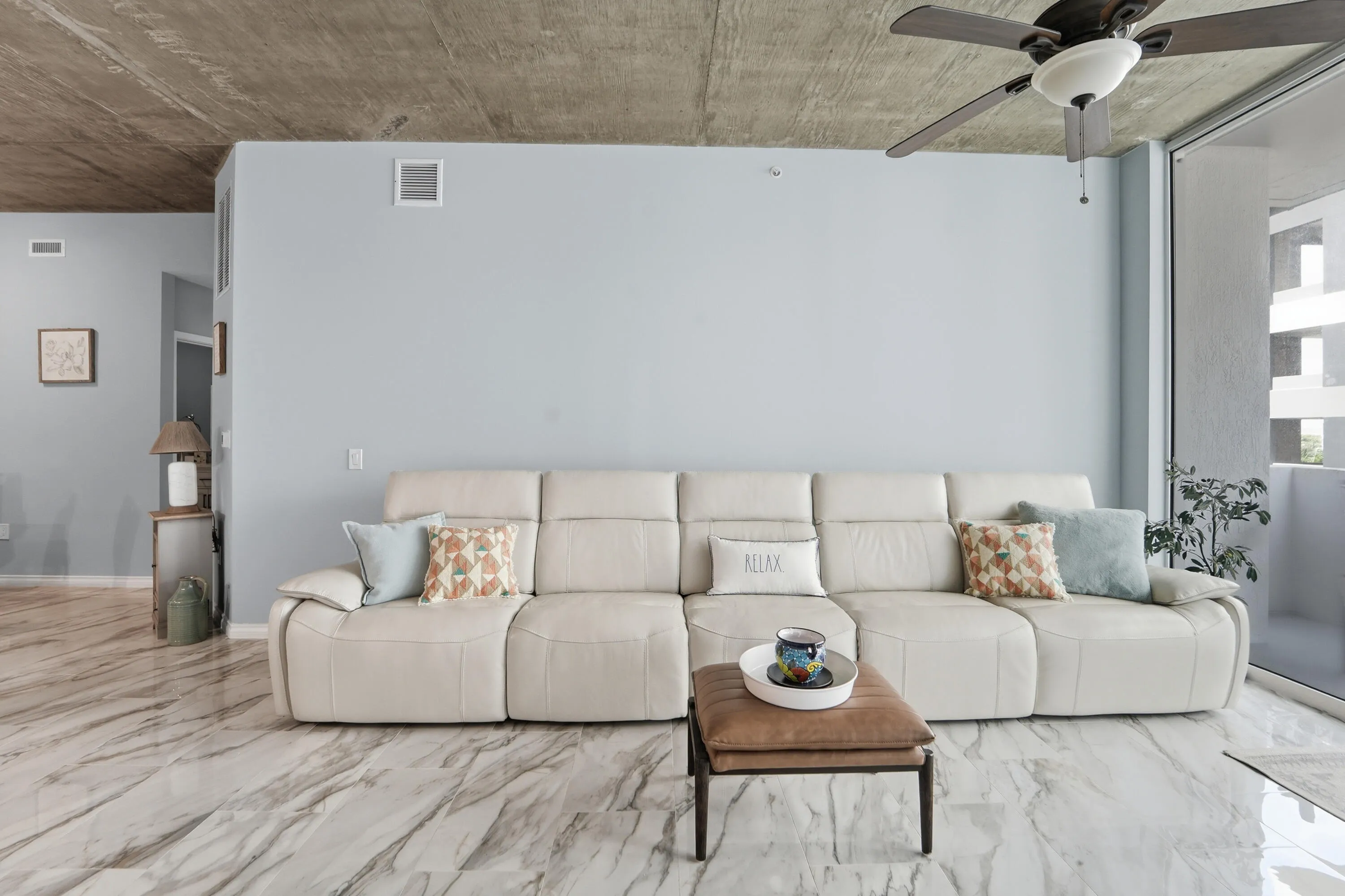 Spacious living area with loft-inspired architecture, floor to ceiling windows, and exposed concrete ceilings