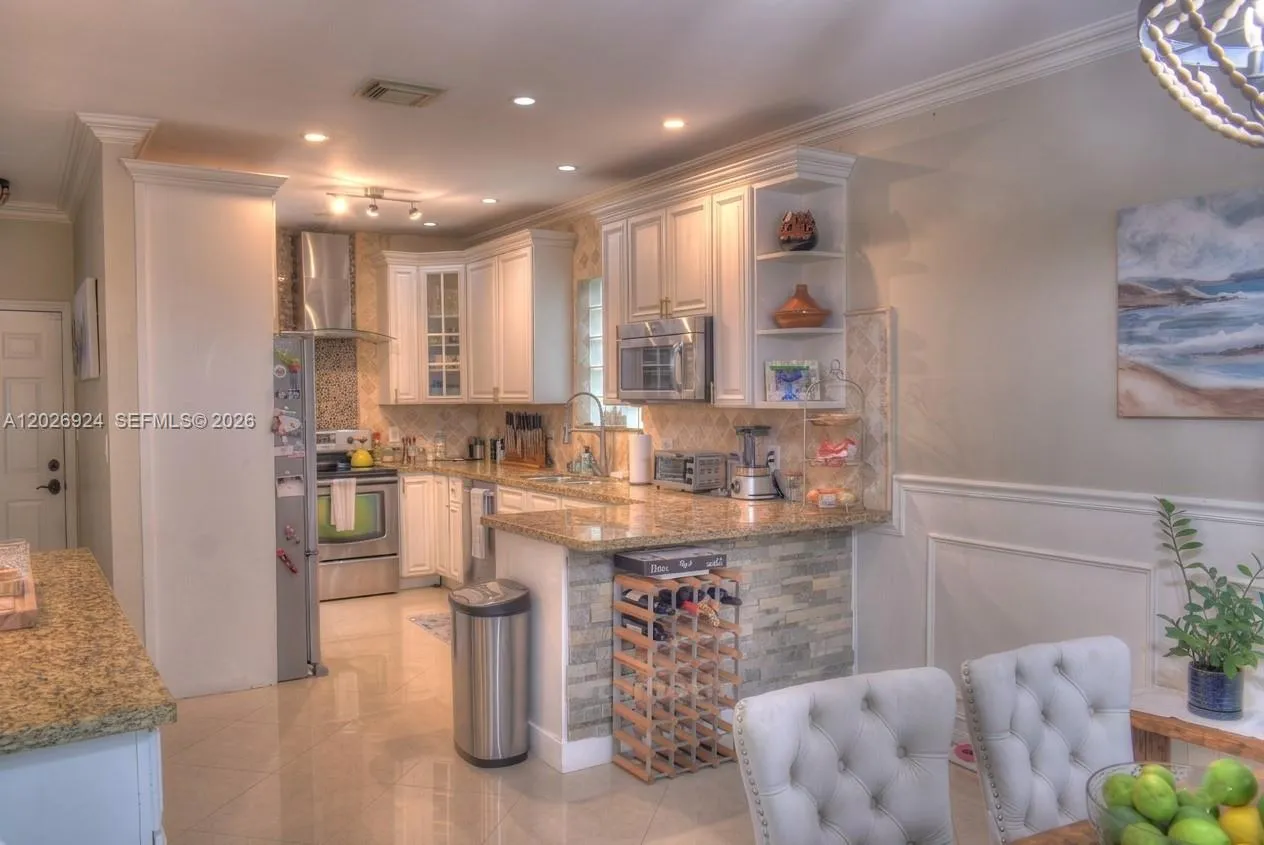 Open kitchen and dining area featuring granite countertops, white cabinetry, stainless-steel appliances, and a comfortable dining space with updated lighting and decorative accents.