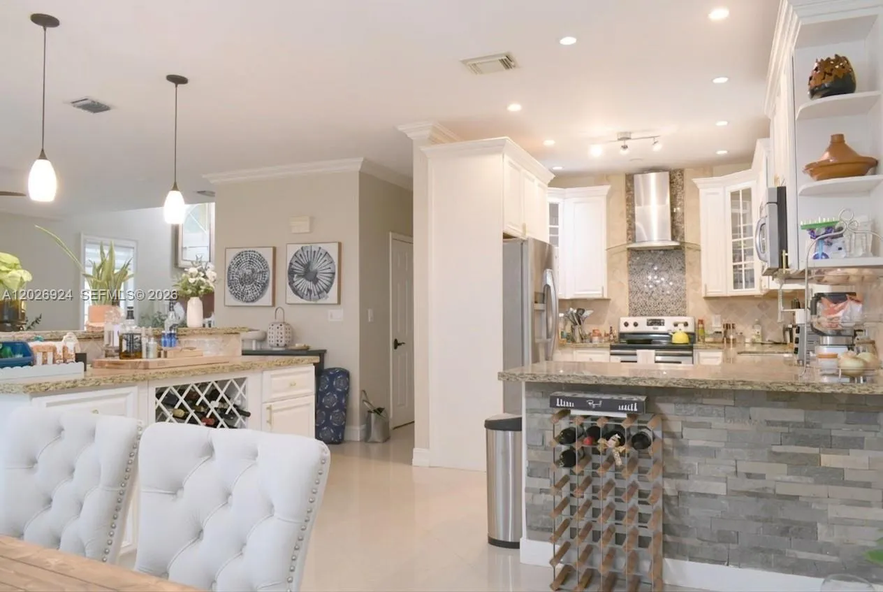 Stylish kitchen area featuring white cabinetry, granite countertops, stainless steel appliances, and a spacious island with pendant lighting—perfect for everyday living and entertaining.