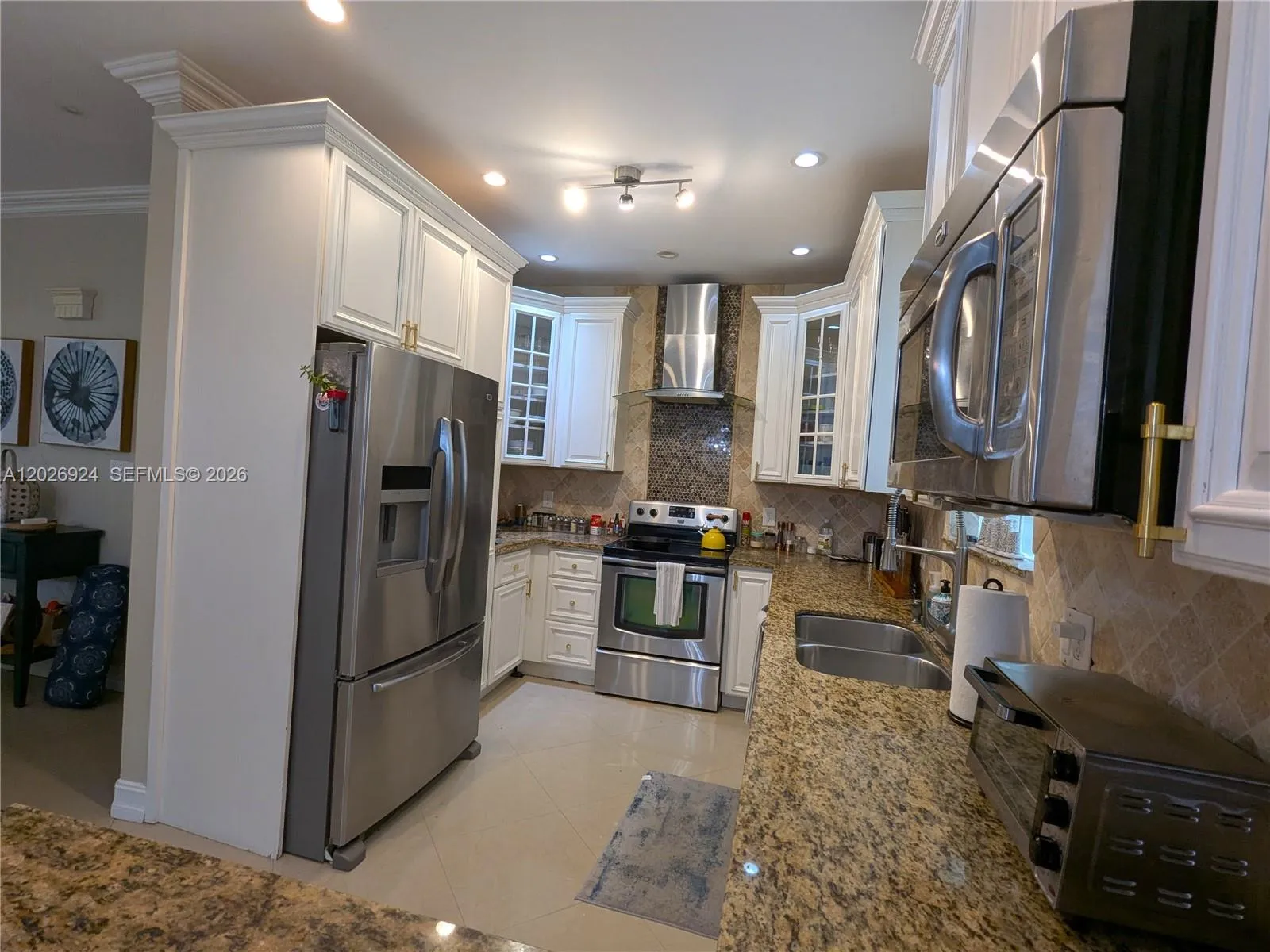 Spacious kitchen with stainless-steel appliances, granite countertops, white cabinetry, accent backsplash, modern hood, and a well-organized layout that highlights both workspace and storage.