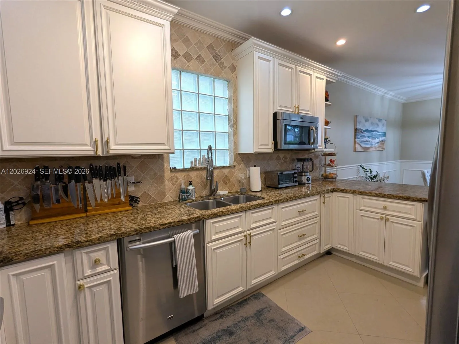 Bright kitchen with white cabinetry, granite counters, stainless-steel sink, and updated appliances, highlighted by a glass-block window that brings in natural light.