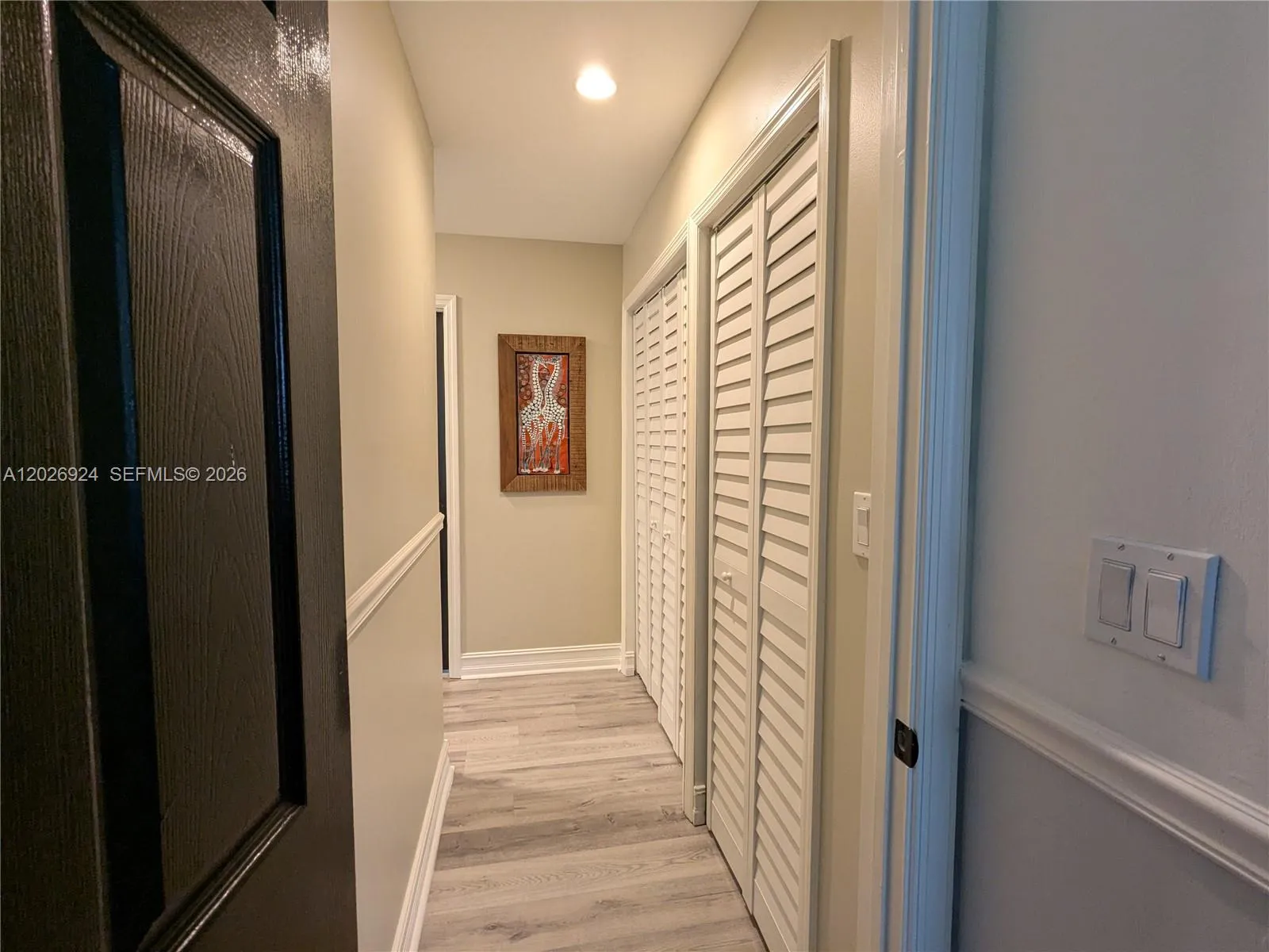 L-shaped and well-lit hallway, featuring wood-style flooring, neutral walls, and organized linen closet space, and air handler closet, creating a neat transition between rooms.