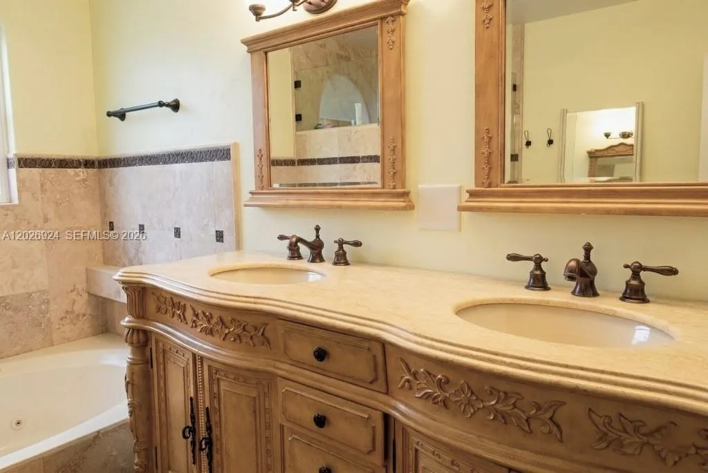 Spacious primary bathroom featuring a double-sink vanity with detailed wood cabinetry, marble countertops, coordinated framed mirrors that highlight the room’s traditional design.