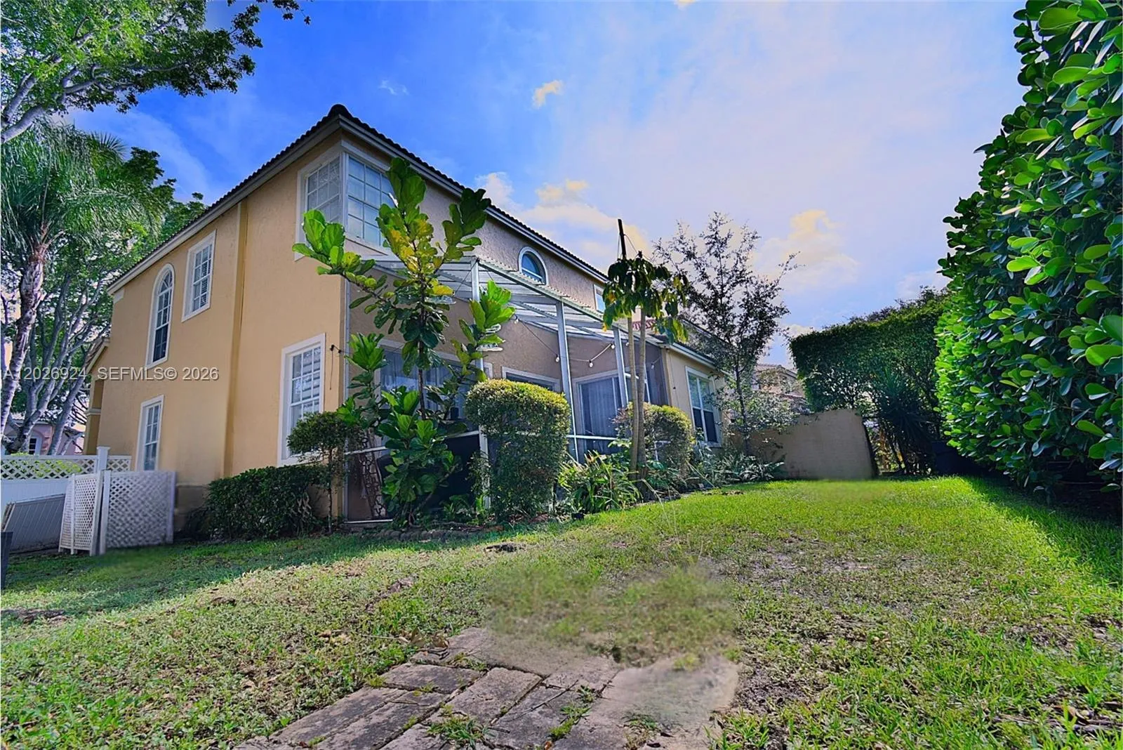 Spacious and well-maintained backyard featuring lush landscaping, mature greenery, and tall hedges that provide excellent privacy. A stone pathway and manicured lawn create a peaceful outdoor setting—perfect for relaxing or enjoying quiet moments in a private, natural environment