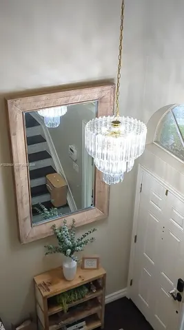 Elegant foyer featuring a crystal chandelier, decorative mirror, and a warm, welcoming entry enhanced by natural light.