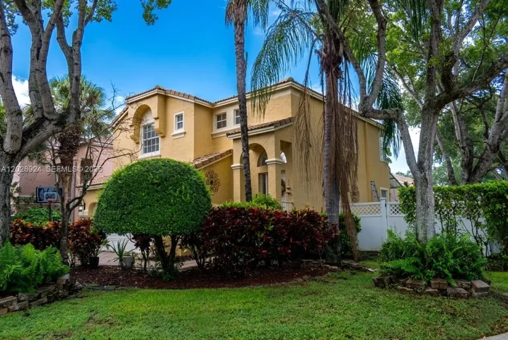 Beautiful Mediterranean-style exterior featuring a tile roof, arched details, and lush tropical landscaping that enhances the home’s curb appeal.