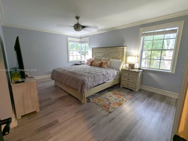 Bright Master bedroom featuring a large bedding area with coordinated décor, modern flooring, ample natural light from dual windows, walk-in closet and master bathroom, creating a comfortable and well-organized retreat.