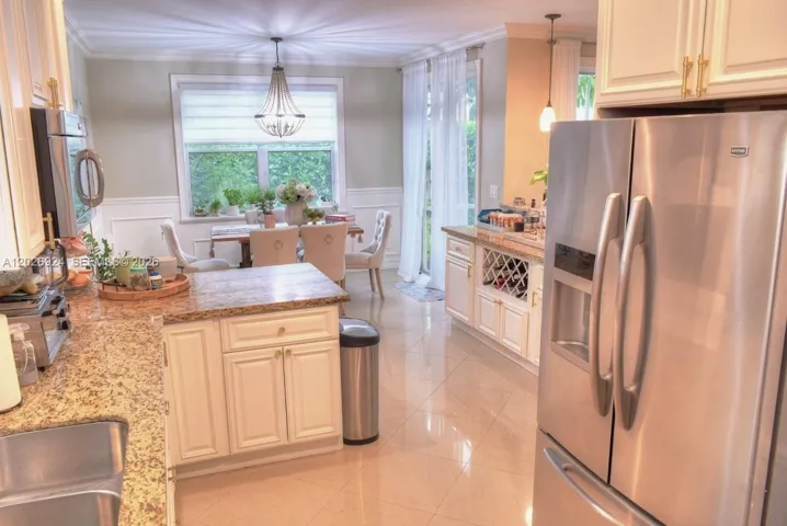 Bright kitchen and dining area featuring white cabinetry, granite countertops, stainless-steel appliances, and a well-lit dining space with large windows and room for elegant seating.