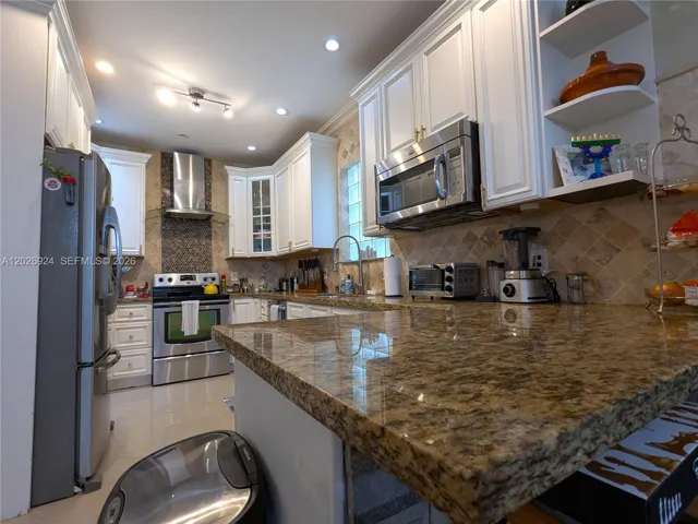 Well-organized kitchen featuring stainless-steel appliances, granite countertops, and ample cabinetry, with additional shelving that provides practical storage and display space, ideal for both workspace and storage.